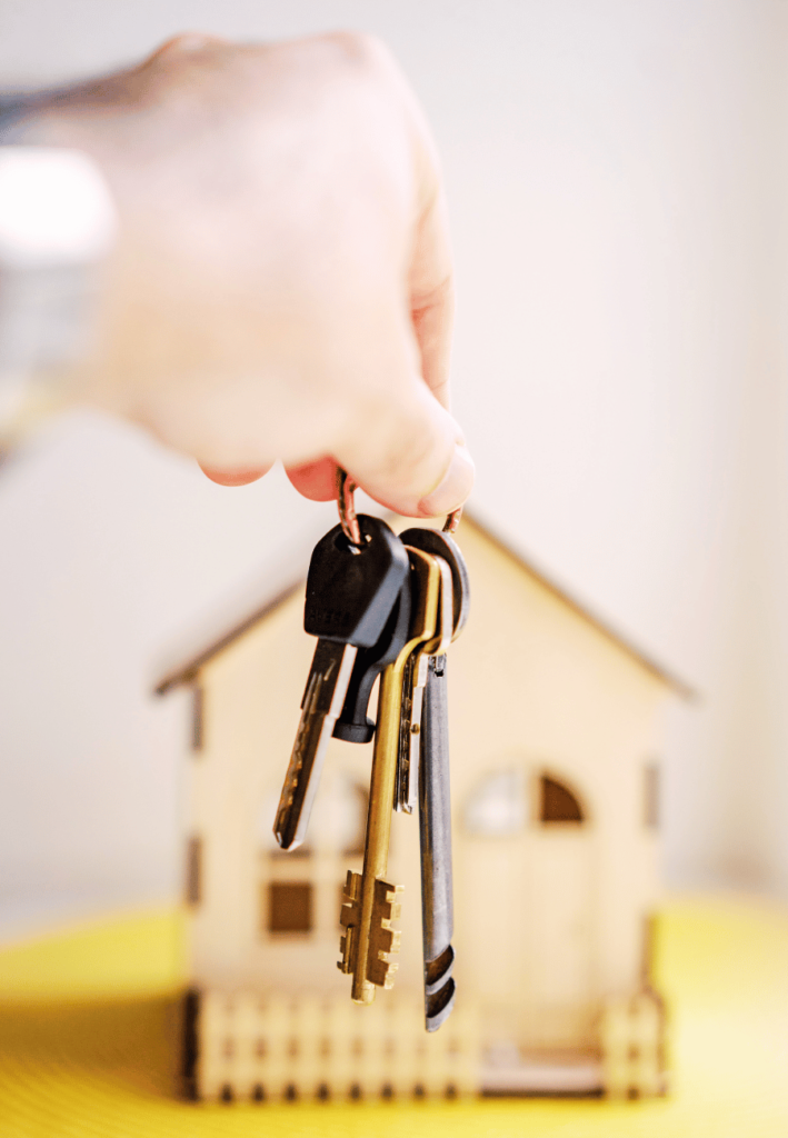 Mano sosteniendo una llave frente a una casa, simbolizando los servicios inmobiliarios de Enigma Corp.